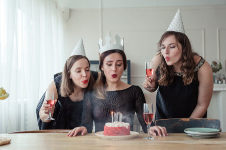 Three women friends celebrating 30s birthday together gathering at table at home with wine and...
