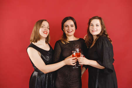 Three 30 years women in black dress with wine glasses over red background. Hen-party, birthday.の写真素材