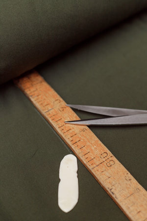 tailor marks up textile using soap and wooden ruler on pattern cutting.
