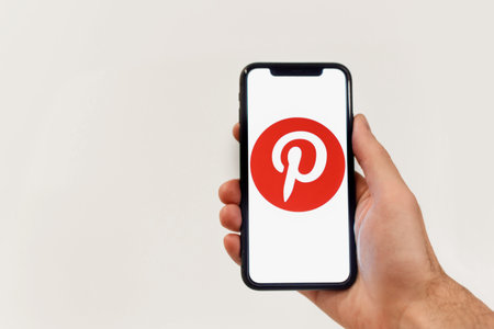 Minsk, Belarus - October 20, 2021: Man hands holding iphone with Pinterest apps logo on isolated on...