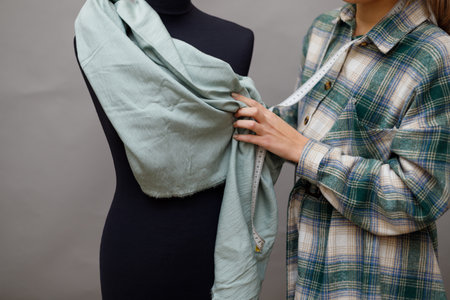 Young woman fashion designer measuring mannequin, seamstress holding tape working with dummy in cozy home or tailor shop, dressmaking and sewing concept, exclusive unique clothes creationの写真素材