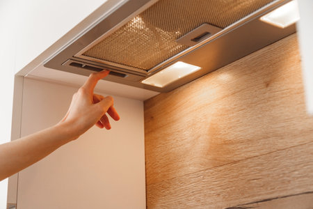 Woman hand turn on embedded cooker hood in white modern kitchen.の写真素材