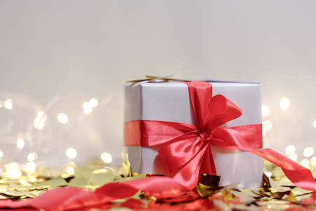 White gift box with red ribbon with golden confetti. Holiday composition card.の写真素材