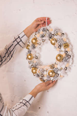 Woman hang modern rustic christmas wreath on wall. Rustic christmas wreath in female hands with fir branches, berries and coneの写真素材