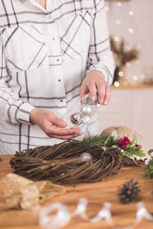 Woman artisan making Christmas holiday wreath on a table among by New Year's decor. Women's hobby. Preparations for the holidays concept. Christmas wreath of cones, spruce branches and toysの写真素材