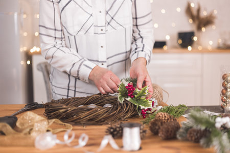 Woman artisan making Christmas holiday wreath on a table among by New Year's decor. Women's hobby. Preparations for the holidays concept. Christmas wreath of cones, spruce branches and toysの写真素材