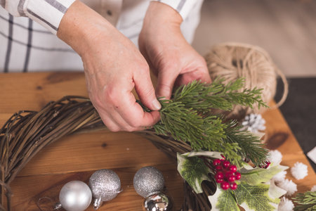 Woman artisan making Christmas holiday wreath on a table among by New Year's decor. Women's hobby. Preparations for the holidays concept. Christmas wreath of cones, spruce branches and toysの写真素材