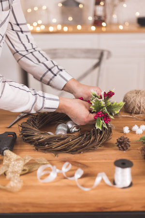 Woman artisan making Christmas holiday wreath on a table among by New Year's decor. Women's hobby. Preparations for the holidays concept. Christmas wreath of cones, spruce branches and toysの写真素材