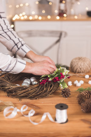 Woman artisan making Christmas holiday wreath on a table among by New Year's decor. Women's hobby. Preparations for the holidays concept. Christmas wreath of cones, spruce branches and toysの写真素材
