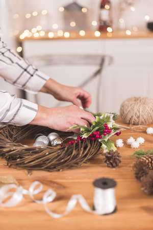 Woman artisan making Christmas holiday wreath on a table among by New Year's decor. Women's hobby. Preparations for the holidays concept. Christmas wreath of cones, spruce branches and toysの写真素材