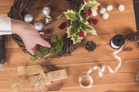Woman artisan making Christmas holiday wreath on a table among by New Year's decor. Women's hobby. Preparations for the holidays concept. Christmas wreath of cones, spruce branches and toysの写真素材