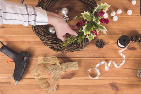 Woman artisan making Christmas holiday wreath on a table among by New Year's decor. Women's hobby. Preparations for the holidays concept. Christmas wreath of cones, spruce branches and toysの写真素材
