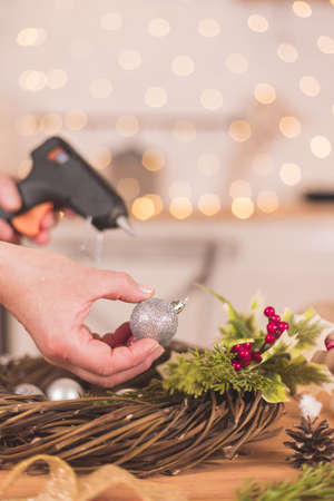 Woman artisan making Christmas holiday wreath on a table among by New Year's decor. Women's hobby. Preparations for the holidays concept. Christmas wreath of cones, spruce branches and toysの写真素材