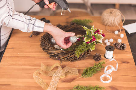 Woman artisan making Christmas holiday wreath on a table among by New Year's decor. Women's hobby. Preparations for the holidays concept. Christmas wreath of cones, spruce branches and toysの写真素材
