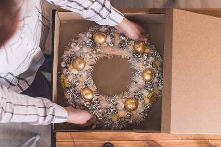 Female artisan is packing a Christmas wreath in a box to be sent to the customer. Delivery, manual work, work with orders. small business conceptの写真素材