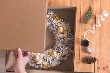 Female artisan is packing a Christmas wreath in a box to be sent to the customer. Delivery, manual work, work with orders. small business conceptの写真素材