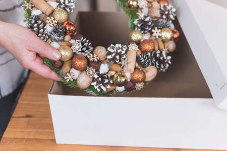 Female artisan is packing a Christmas wreath in a box to be sent to the customer. Delivery, manual work, work with orders. small business conceptの写真素材