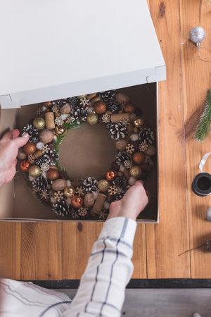 Female artisan is packing a Christmas wreath in a box to be sent to the customer. Delivery, manual work, work with orders. small business conceptの写真素材