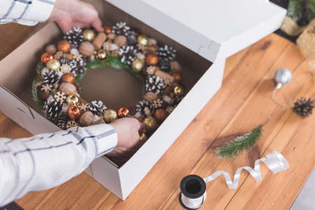 Female artisan is packing a Christmas wreath in a box to be sent to the customer. Delivery, manual work, work with orders. small business conceptの写真素材