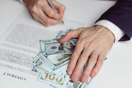 Man in suit signing a contract and holding hand on moneyの写真素材