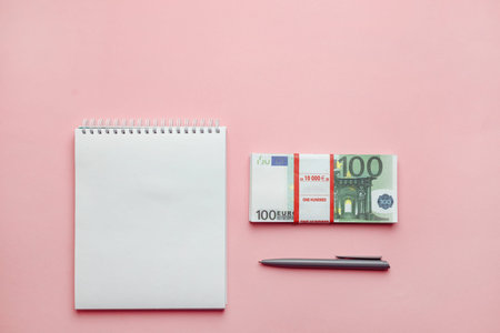 Investment and budget planning concept. Notepad, pen and bundle of money on a pink background. Mitimalism. Top view flat lay.の写真素材