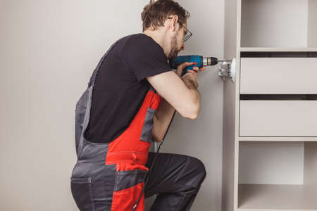 Furniture assembler drilling holes to fix sliding pants hanger in wardrobeの写真素材