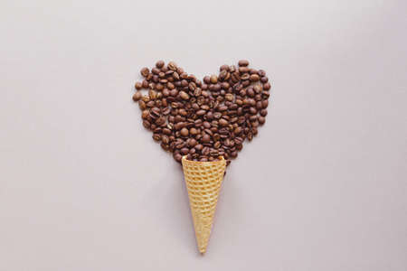 Roasted coffee beans in shape of heart in wafer or waffle cone for ice cream on color background, copy space. coffee love conceptの写真素材