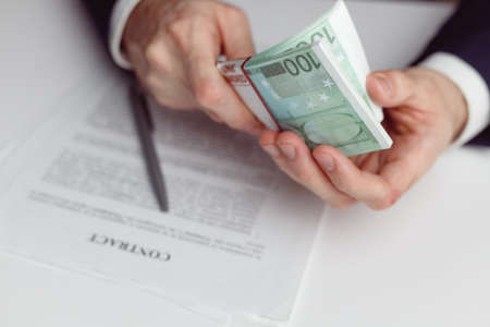 Man in suit counts wad of money before signing contract. Close up of hands with money euroの写真素材