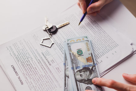 Man signing real estate contract, making a deal with cash dollar money and home keys. Buying or...