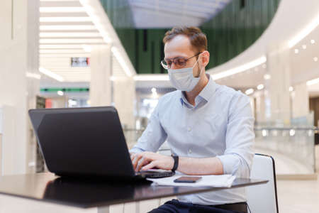 Clerk in face mask man working remotely on laptop in a public placeの写真素材