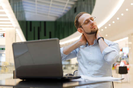 Man warming up his neck during the working at laptop. businessman freelancer working at mall. Prevention of health problems from working at the computerの写真素材