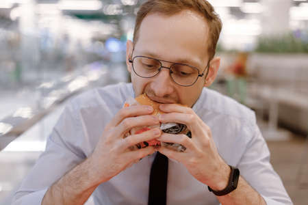 Office worker eating fast food burger and drink soda at food court in mall at lunchの写真素材