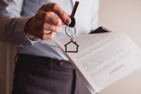Manager offers keys to house holding contract in other hand. Renting and buying a property