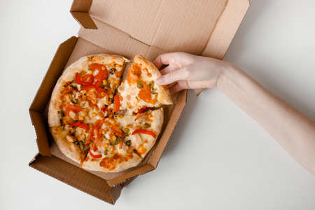 Female hand take piece of mexican pizza in cardboard box for delivery on white solid background. top viewの写真素材