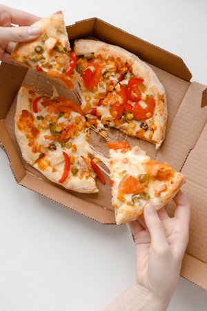 Female hand take piece of mexican pizza in cardboard box for delivery on white solid background. top viewの写真素材