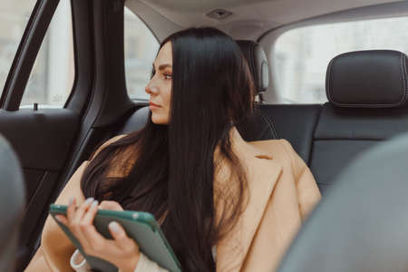 Young european businesswoman portrait inside taxi using tablet.の写真素材