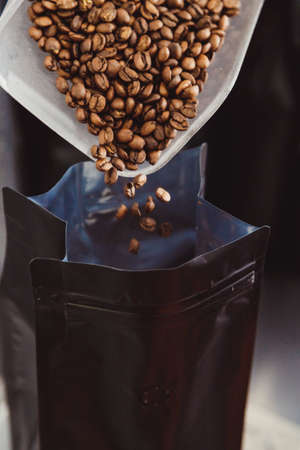 Man scales roasted coffee beans, pour into package for saleの写真素材