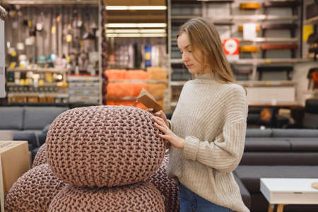 Young caucasian woman buyer choosing knitted pouf in furniture shop.の写真素材