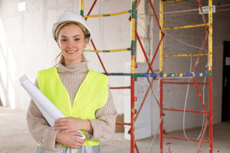 Woman architect in protective helmet with paper project on construction site. Looking at camera half half-height portrait of female foreman at construcionの写真素材