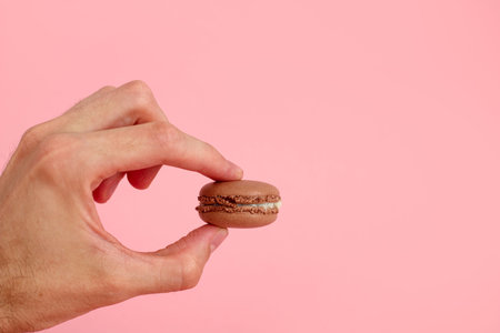 Chocolate macaron on fingertips, french cookies on a plain pink background.の写真素材