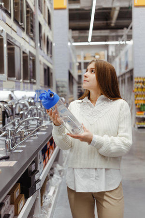 Woman holds household water filter for purification from mechanical impurities in hardware store. Repair of the water supply system at home, purchase of a filter. Woman in plumbing sectionの写真素材