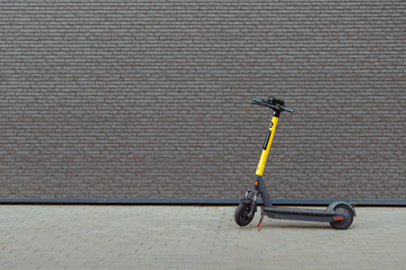 Electric kick scooter at black brick wall, contemporary city transport, sharing. Urban style, no people.の写真素材