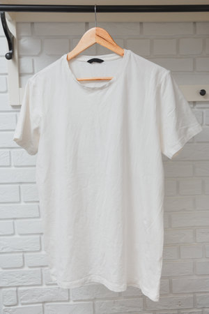 Mock-Up of White Cotton T-Shirt on Wooden Hanger with white interior in backdrop.の写真素材
