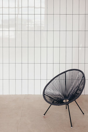 Wicker string chair against white ceramic tile wall. Minimal interior.の写真素材
