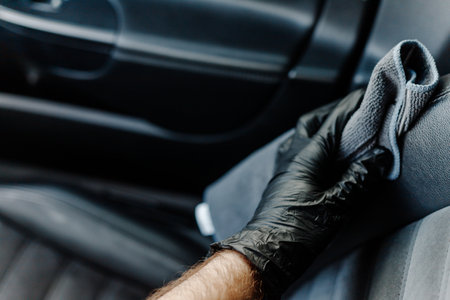 Mans hand in black glove cleaning car interior, dashboard and leather seats with microfiber clothの写真素材