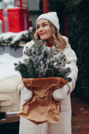 Woman in white hat and winter fur coat with pine branch in city, lights and decorations on background.の写真素材