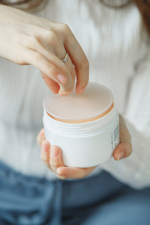 Womans hands opening new skin care cosmetic jar. Minimalism. Close up view on white jarの写真素材