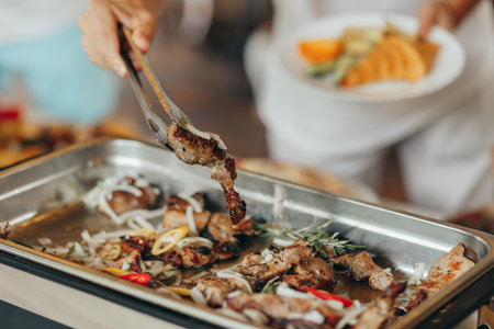 catering, food and people concept - close up of female hands with tongs preparing shish kebabの写真素材