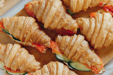 Croissants with cheese cream, red fish and cucumber on wooden board, picnic or outdoors cateringの写真素材