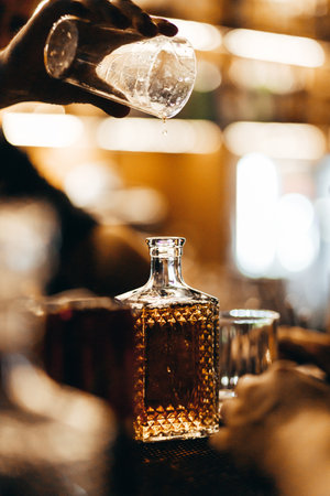 A bartender pours whiskey from a measuring glass into a decanterの写真素材